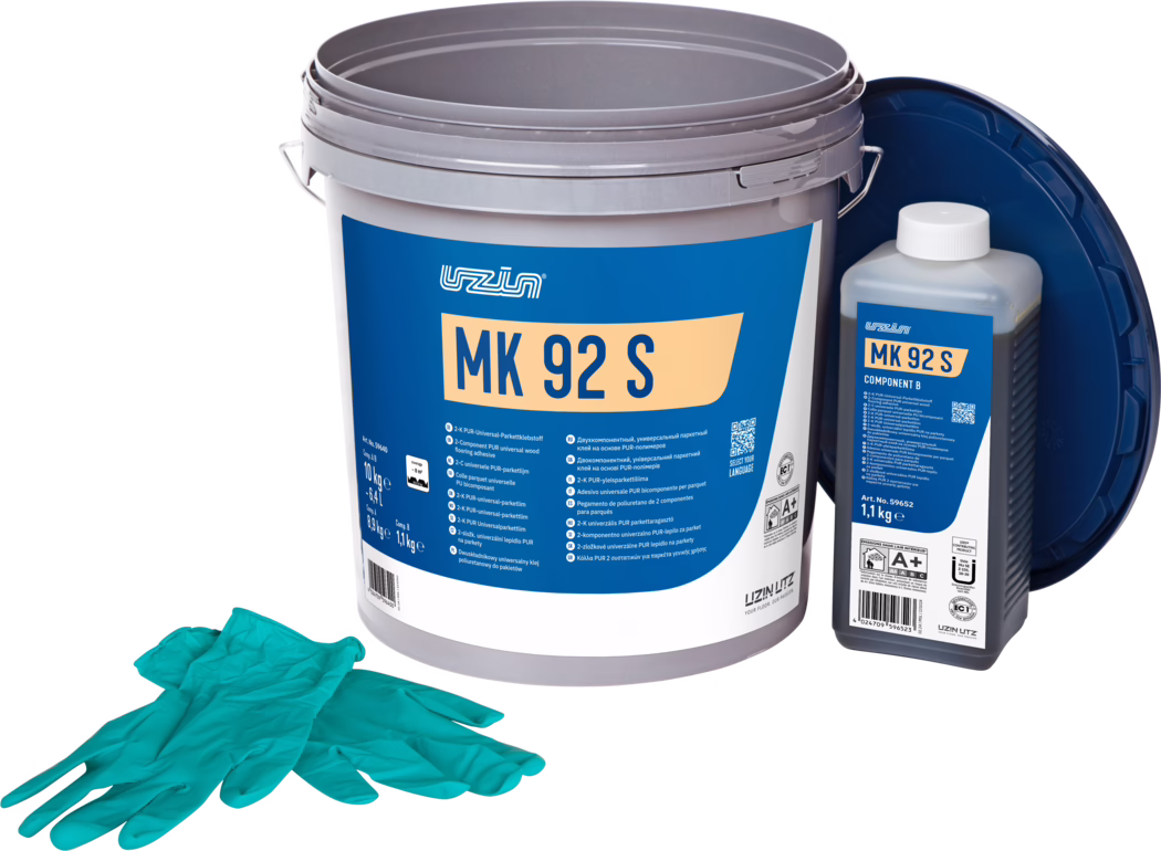 UZIN_Dummy_MK 92 S-10kg_2024-09 Produkční fotografická snímek lepicí sady na parkety: velký šedý plastový kbelík s výraznou modrou etiketou 'MK 92 S', vpravo menší obdélníková lahev s nápisem 'MK 92 S Component B' a bílým víčkem, za nimi se opírá tmavě modré víko. V popředí leží pár tyrkysových jednorázových rukavic. Předměty jsou uspořádány na bílém pozadí a rovnoměrně osvětleny, zdůrazňují detaily obalu a informace o produktu pro pokládku podlahy.